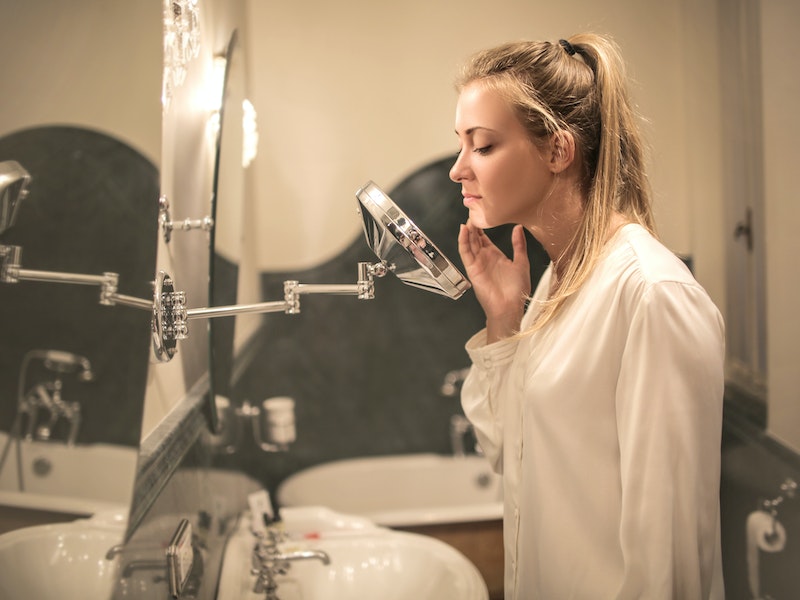 Upset woman examining skin in small mirror Upset woman examining skin in small mirror